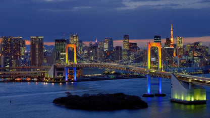 View of the iconic Rainbow Bridge in Odaiba, Tokyo, illuminated at night with vibrant colors. The bridge spans across Tokyo Bay, offering stunning views of the city skyline and waterfront